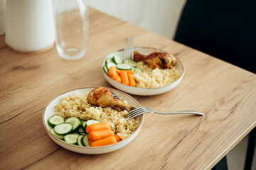 Bulgur, fresh vegetables and chicken drumstick on a plate for lunch at home.