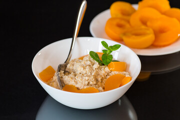Oatmeal with canned peaches and mint, isolated on black background