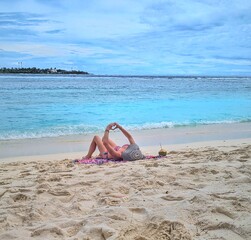 A woman lies peacefully on the white sand of a Maldives beach, enjoying the tropical sunshine