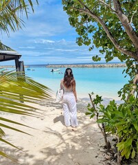 A woman strolls down a tropical path towards the white sand beach and clear waters of the Maldives