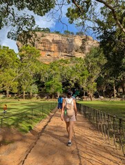 A woman walks towards the iconic Sigiriya Rock in Sri Lanka, surrounded by lush greenery and ancient history