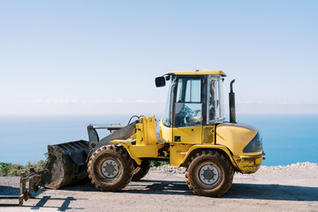 Yellow excavator stands on a steep seashore. Side view