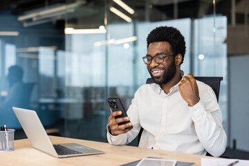 Successful businessman celebrating victory and triumphant achievement results. Man with phone in...