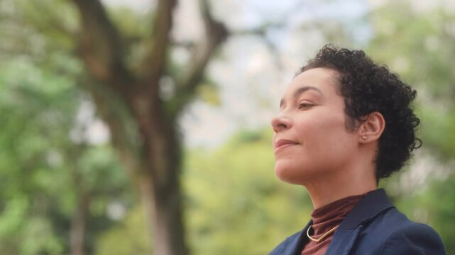 Confident Brazilian woman in business attire admiring the city with a thoughtful smile. Professional with short curly hair appreciating urban environment in close-up shot.