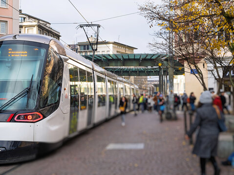 Strasbourg, France - Dec 12, 2022: A modern tram arrives at Place de l'Homme de Fer in Strasbourg as commuters walk along the cobblestone street, surrounded by urban architecture and seasonal trees