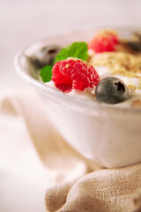 Muesli mit Obst in weisser Schale und hellem Tuch, Frühstück, Himbeere, gesund, Milch, 