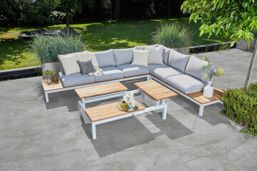 3D Render of Inviting Modern Outdoor Living Space with L-Shaped Sofa, Wooden Accent Tables, and Lush Green Surroundings