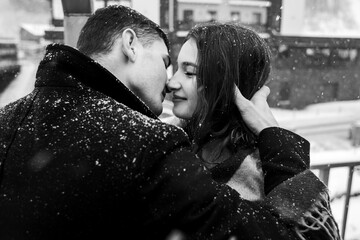 A black and white photograph showing a couple standing close to each other on the street. The man...