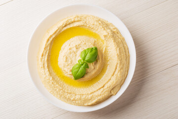 Top view on homemade hummus with olive oil in a white bowl on a light wooden background. Traditional Arabic snack.