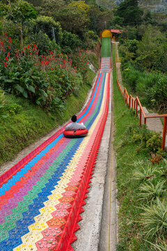 Young man riding at colorful rainbow plastic slide at the extreme adventure park in the mountain rainforest in El Salvador.