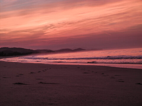 amanecer o atardecer en una playa con olas y brisas con cielo rojizo, nubescoloridas y agua de mar reflejando el cielo