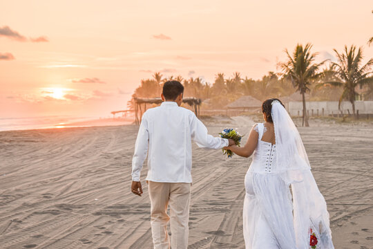 novios caminando en la orilla de la playa en un atardecer de boda romantica