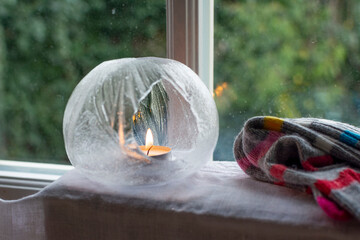 An Ice Lantern with candle in front of a window.