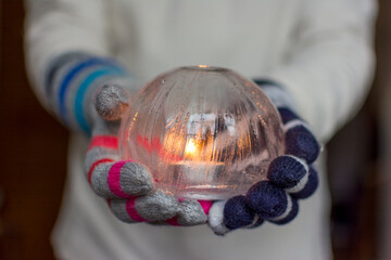 Gloved Hands Holding an Ice Lantern with candle in front of a window.