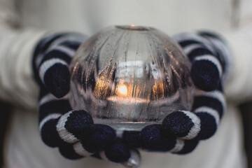 Gloved Hands Holding an Ice Lantern with candle in front of a window.