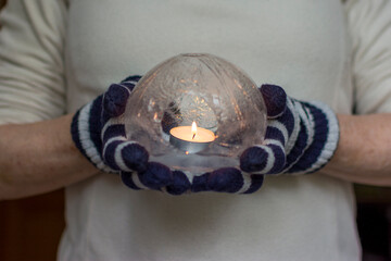 Gloved Hands Holding an Ice Lantern with candle in front of a window.