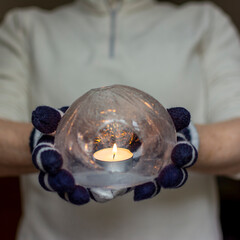 Gloved Hands Holding an Ice Lantern with candle in front of a window.