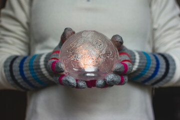Gloved Hands Holding an Ice Lantern with candle in front of a window.