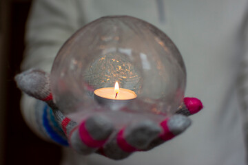 Gloved Hands Holding an Ice Lantern with candle in front of a window.