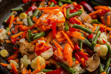 Bright multi-colored vegetables stewing in a frying pan close-up