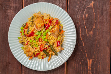 On a wooden table in a plate there are vegetables stewed with bulgur