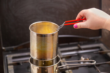 French fries in boiling oil in a mini deep fryer on the stove in a home kitchen