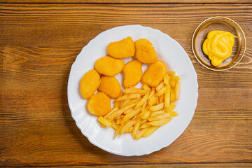 French fries and golden nuggets with cheese sauce on a small wooden table