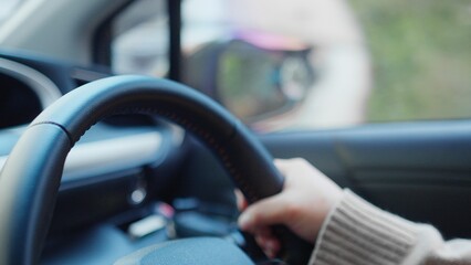 A close-up view of a hand gripping a steering wheel inside a modern car, showcasing the interior...