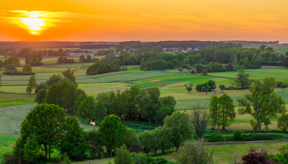 landscape of the Polish countryside, beautiful green fields and meadows by a small river, evening sunset with colors in the sky