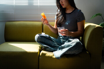 Young woman taking medicine pills sitting on the sofa at home