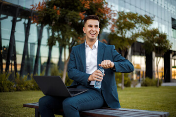 Fototapeta premium Man Sitting on Bench with Laptop and holding a bottle of water