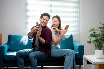 Obraz premium Happy couple is using smartphones sitting on sofa, enjoying social media and having fun together at home