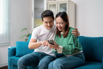 Young asian couple using smartphone sitting on sofa at home