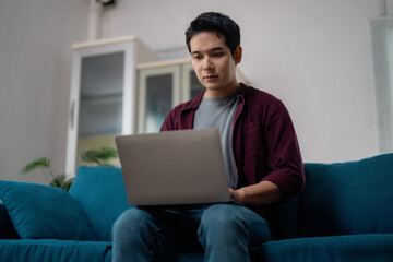 Young man working from home sitting on sofa using laptop