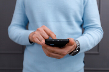 Person using a smartphone in a casual setting while wearing a light blue sweater