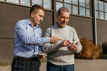 Two Men Review Data on a Tablet in Front of a Building on a Sunny Day