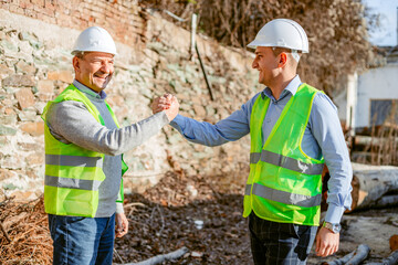 Two Construction Workers Shake Hands In Front Of Brick Wall