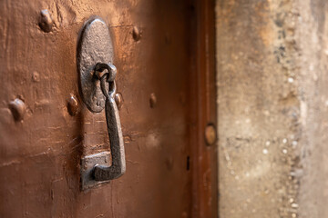 close-up of an antique metal door knocker on a weathered brown wooden door with metal rivets. rustic texture historical charm and craftsmanship of old European architecture old wall