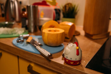 Kitchen timer in the form of a rooster. In the background there is a cutting board, a pumpkin and a...