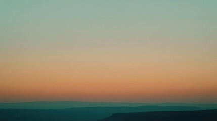 Fototapeta premium A serene landscape at dusk with gentle hills fading into a gradient of soft turquoise and warm peach hues.