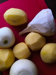 peeled potatoes onions and parsnips on a red board