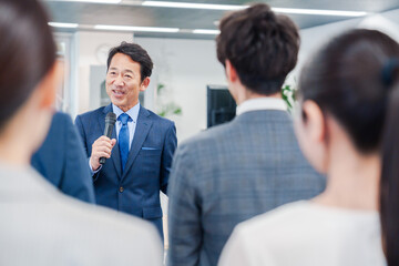 オフィスでの朝礼で挨拶をする管理職の男性