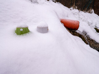 A snowy landscape with a small water source flowing from an orange pipe onto the rocks. Two...
