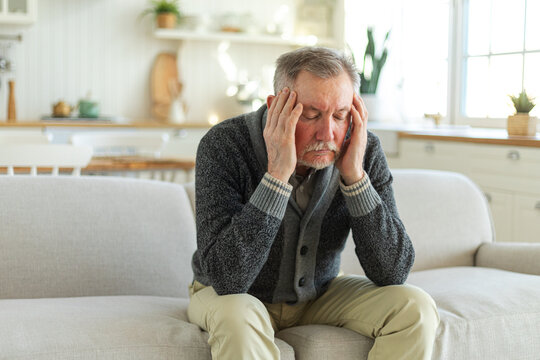 Headache pain. Unhappy middle aged senior man suffering from headache sick rubbing temples at home. Mature old senior grandfather touching temples experiencing stress. Man feeling pain hurt in head