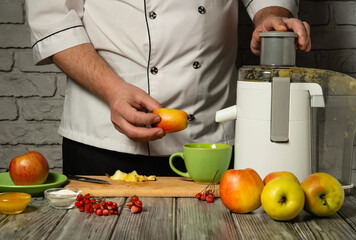 Experienced chef in white uniform adding sliced apples to electric juicer. Making delicious and healthy apple juice in restaurant or hotel kitchen for dinner. Apple diet