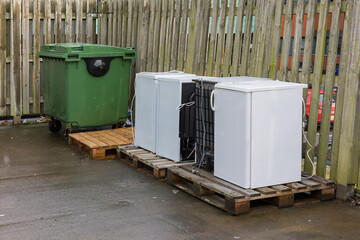 Appliance Disposal: Old Refrigerators and Freezers on Pallets with Green Wheelie Bin Dumpster