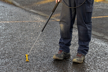 Gas Engineer Wearing PPE Using Long Handle Combustible Gas Leak Detector With Yellow Probe at Ground Level in City Street