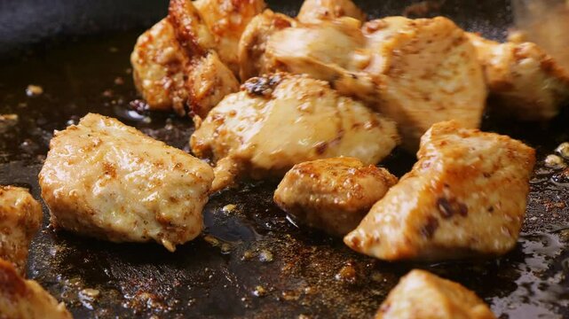 Onions and chicken pieces are fried in vegetable oil with spices and sauce in a hot frying pan. Medium shot.