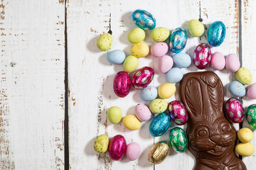 Chocolate Easter bunny with mini Easter eggs on white wooden background. With copy space.