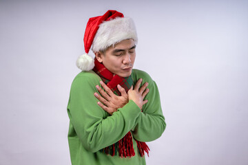 An Asian man wearing a Santa hat, green sweater, and red plaid scarf playfully hugs himself with a warm, cozy expression. He conveys a humorous and festive mood against a white background